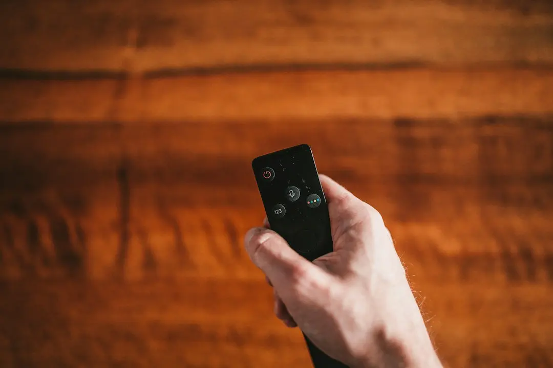 A hand holding a small streaming-device remote in front of a wooden wall, ready to set up Glomax8K on a Fire TV Stick