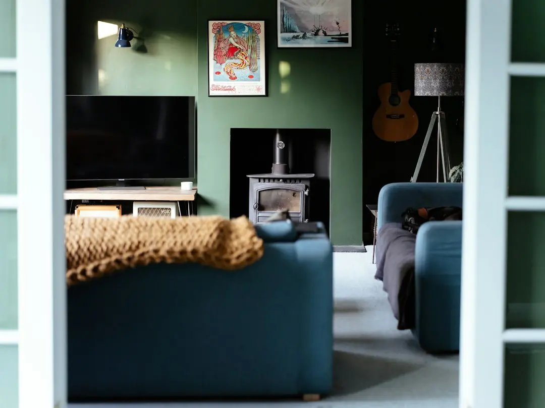 A green-walled living room with a blue sofa, a wood stove and a switched-off TV, the kind of home where Glomax8K IPTV is watched